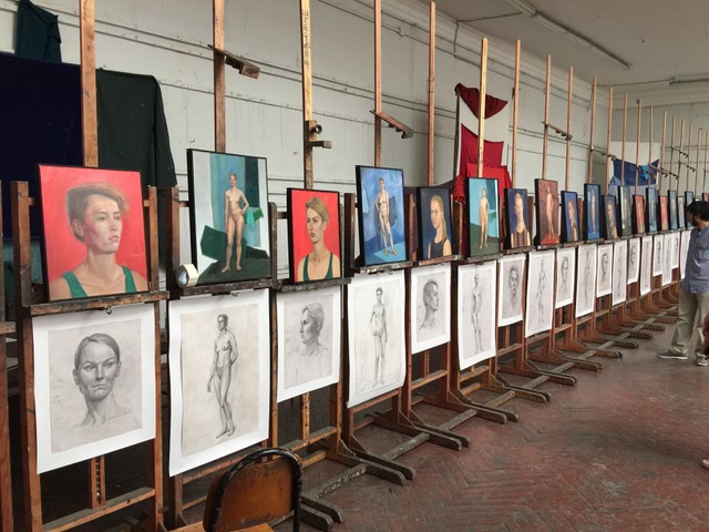 A photo of many graphite and oil painting figure studies lined up on easels.